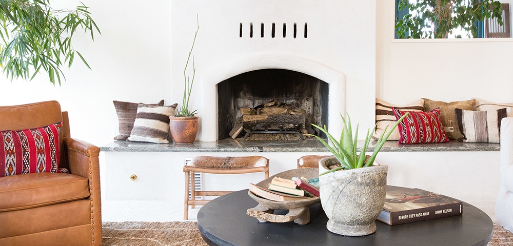 Interior family room designed by Nantucket Home with cowhide bench, kilim pillows, succulents and stucco fireplace